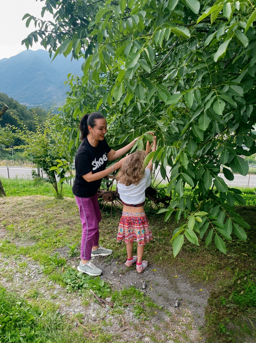 Donna e bambina che raccolgono noci sotto un albero con montagne sullo sfondo